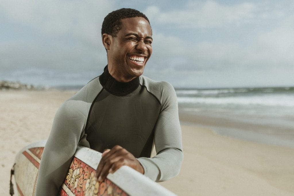 man-smiling-on-beach-with-surfboard